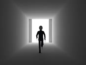 暗い通路の先にある明るい出口の光に向かって走る人物のシルエット