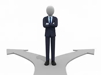 左右二手に分かれた道の分岐点に腕を組んで立っているスーツ姿のビジネスマン