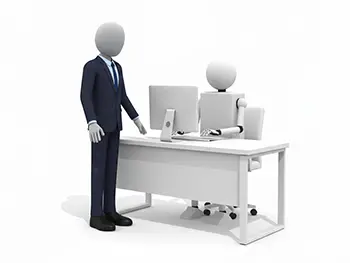 デスクでパソコン作業をするロボットの横に立つスーツ姿のビジネスマン