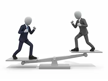 シーソーの両端に乗り、ファイティングポーズで向かい合う二人のスーツ姿のビジネスマン