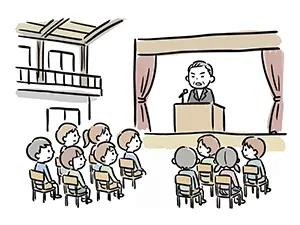 体育館のステージで挨拶する校長先生とパイプ椅子に座って話を聞く新入生たちのイラスト